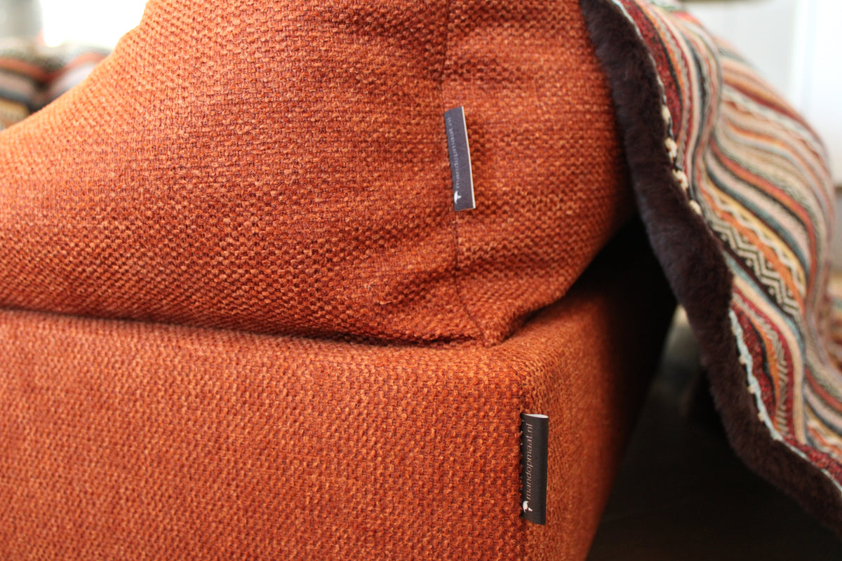 Detail van een maatwerk hondenbed met roestkleurige bekleding en een deken van imitatiebont en gobelinstof